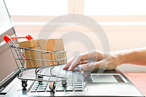 Many parcel boxes in a shopping cart , woman`s hand using a laptop computer  for online shopping concept