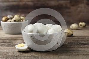 Many peeled hard boiled quail eggs in bowl on wooden table, closeup
