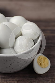 Many peeled hard boiled quail eggs in bowl on wooden table, closeup