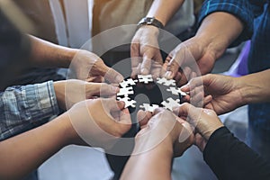 Many people hands holding a jigsaw puzzle in circle together