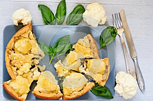 Many pieces of healthy cauliflower pie on the gray plate decorated with fresh basil leaves and vintage silver knife and fork
