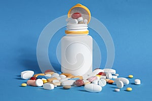 Many pills spilled from a plastic bottle. Multicolored pills spilling out of a plastic bottle on a blue background