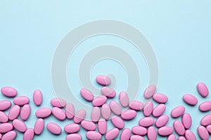 Many pink dragee candies on light blue background, flat lay. Space for text