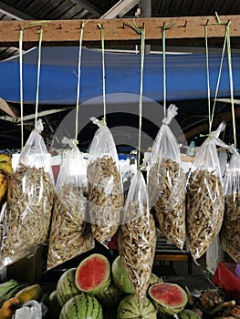 Many plastic bag of dry small anchovy fish hanging on the wooden rack at farmer market.