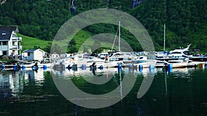 Many pleasure boats and their reflections in the fjord water at the marina in Geiranger, Norway near a steep mountain