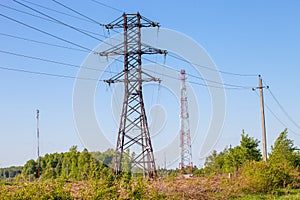 Many power poles, wires, communication towers, antennas against the background of spring nature and the blue sky