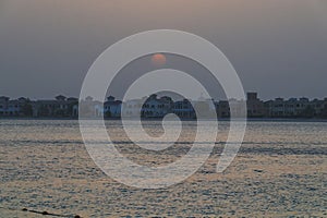 Many private houses above the waters of the sea, over which the sun sets, hiding in the evening haze. The sun over private houses.