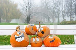 Many pumpinks with painted faces on white porch.