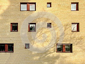 Many random placed windows on a yellow brick residential building outdoors.