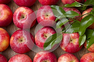 Many red apples with leaves on a wooden background