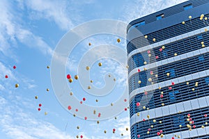 Many red and gold balloons fly beside buildings with blue sky and white clouds