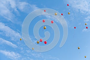 Many red and gold balloons fly under the blue sky and white clouds