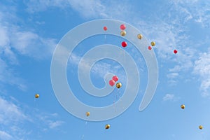 Many red and gold balloons fly under the blue sky and white clouds