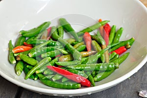 Many red and green Thai Chillis in plate on wooden table.