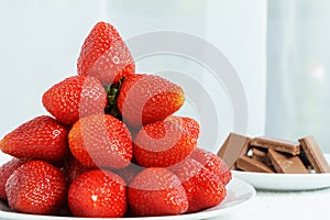 Many red ripe jucy strawberry at white plate close to cup of chokolate on table in light room