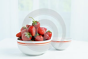 Many red ripe jucy strawberry at white plate close to cup of sour cream on table in light room