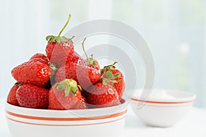 Many red ripe jucy strawberry at white plate close to cup of sour cream on table in light room