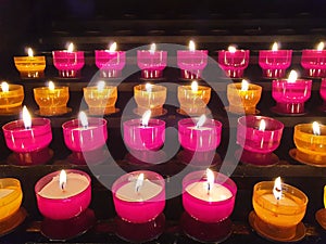 Many Red and yellow glowing prayer candles inside a catholic church on a candle rack