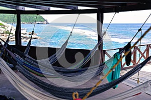 Many relaxing hammocks under a bungalow, with a blurred ocean background in Tairona National Park, Colombia photo