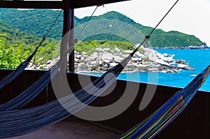 Many relaxing hammocks under a bungalow, with a blurred ocean background in Tairona National Park, Colombia