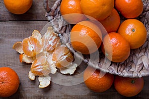 Many ripe mandarins in a basket. One peeled and divided into lobules