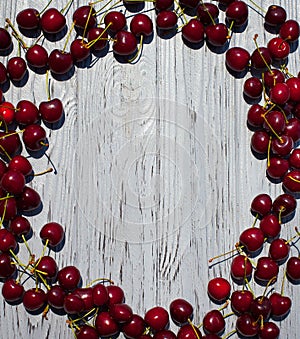 Many ripe red cherries on the branches lie in the form of a frame along the edges of a light wooden table