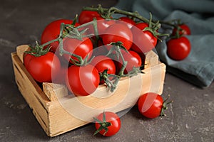 Many ripe red tomatoes in wooden crate on grey table