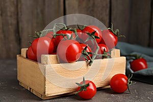 Many ripe red tomatoes in wooden crate on grey table