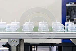 Many  row of clear plastic cup or box after made by plastic injection mold machine on automatic conveyor belt during manufacturing