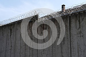 many rows of barbedwire, high concrete fence, barbed wire fence on top, building for execution of punishments for criminals,