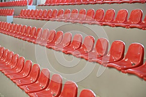 Many rows of red plastic seats in a grandstand stadium in the fresh air, day and light