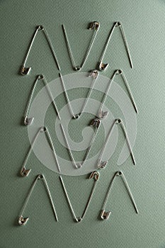 Many safety pins on green background, flat lay