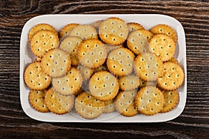 Many salted crackers in white plate on wooden table. Top view