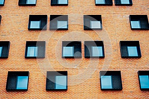 Many same quadratic windows on a modern brown brick building in daylight. Architecture concept. Strange window