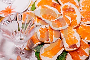 Many sandwiches with butter and red fish lie on a plate near a crystal champagne glass