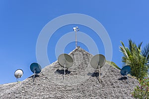 Many satellite antennas on a thatched roof against a blue sky on the island of Zanzibar, Tanzania, Africa