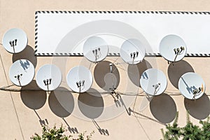 Many satellite dish antenna hanged on building wall with big white empty signboard banner on background. Copyspace for