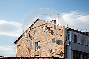 Many satellite dish antennas on the home wall. Brick house and satellite dishes in a small town