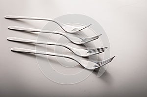 Many shiny gourmet restaurant quality design silver forks laying elegant in a row on a white dining table with copyspace