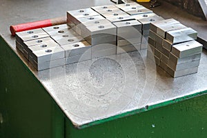 Many shiny metal, iron rectangular blanks with drilled holes, metalwork tools and industrial grips on the robotic green table in t