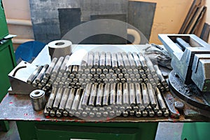 Many shiny metal studs with carving, nuts, iron rings, gaskets, metalwork tools and industrial vice on the table in the factory