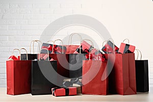 Many shopping bags with gift boxes on table against white brick wall. Black Friday sale