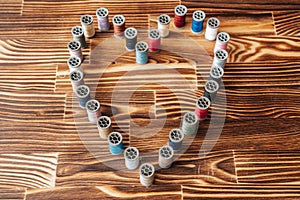 Many side by side aline thread spools in a heart shape on a wooden background.