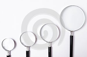 Many sizes of magnifying glass on white table,top view