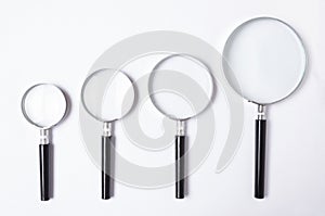 Many sizes of magnifying glass on white table,top view