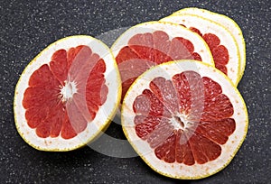 Many sliced fresh grapefruits on black background, top view