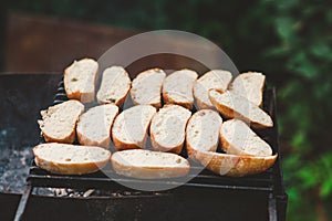 Many slices of roasted baguette bread on a grill over fire on fresh air