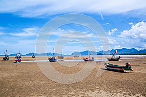 Many small fishing boats on sand beach during low tide with cloudy blue sky