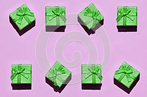 Many small green gift boxes on texture background of fashion trendy pastel pink color paper