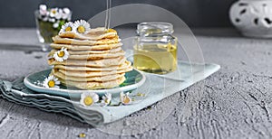 Many small pancakes with honey or syrup. Delicious traditional breakfast. Spring flowers as food styling in photography. Gray